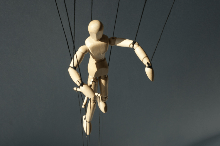 Houten pop aan touwtjes tegen een grijze achtergrond; beeld voor een manager die gestuurd wordt in plaats van leidt.