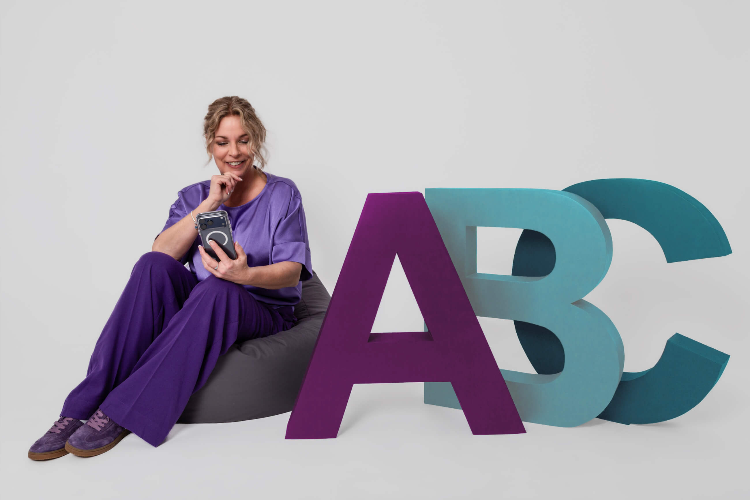 Claudia Bouwens met telefoon naast ABC-letters in huisstijlkleuren (reviews)