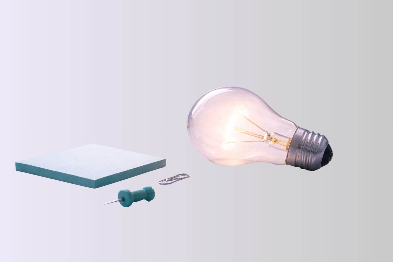 Brandende lamp naast notitieblaadje, paperclip en punaise als symbool bij inspiratiesessies voor nieuwe ideeën, richting en beweging.