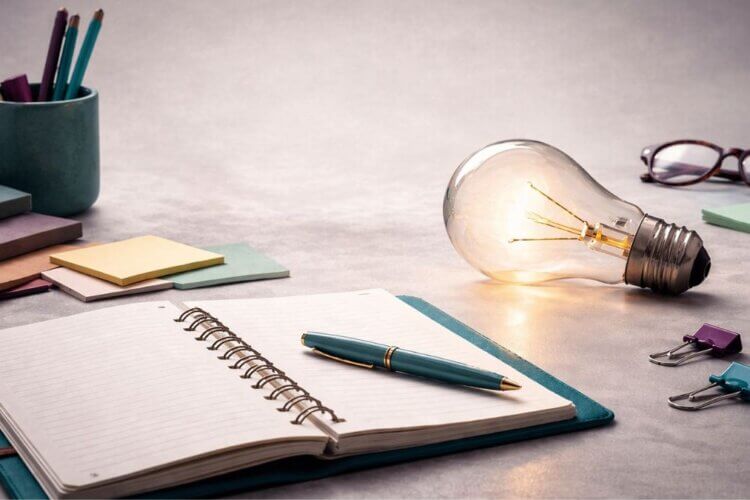 Brandende lamp naast een open notitieboek en pen als symbool voor een inspiratiesessie die nieuwe energie, inzicht en beweging brengt